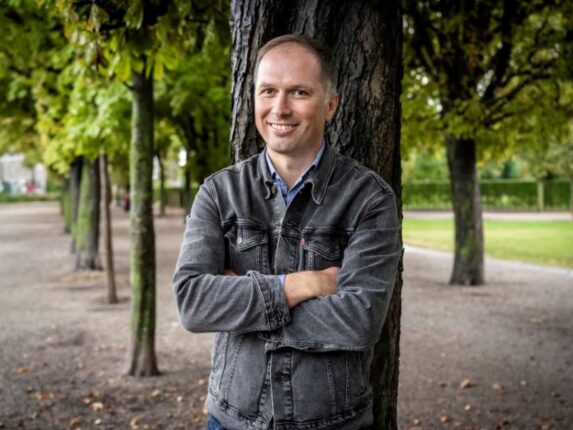 Bernhard Seitz, Bezirksvorsteher-Stellvertreter, steht im Augarten im Herbst 21 in einer Allee, an einen Baum gelehnt.