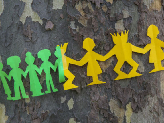 Papierfiguren in Grün und Gelb rund um einen Baumstamm