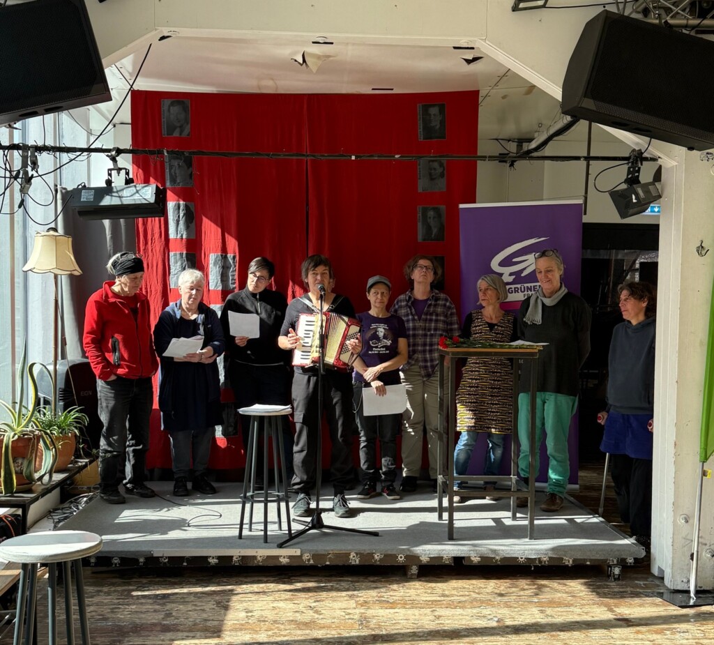 Maren Rahmann mit Ziehharmonika, hinter ihr mehrere Sängerinnen des feministischen Chors