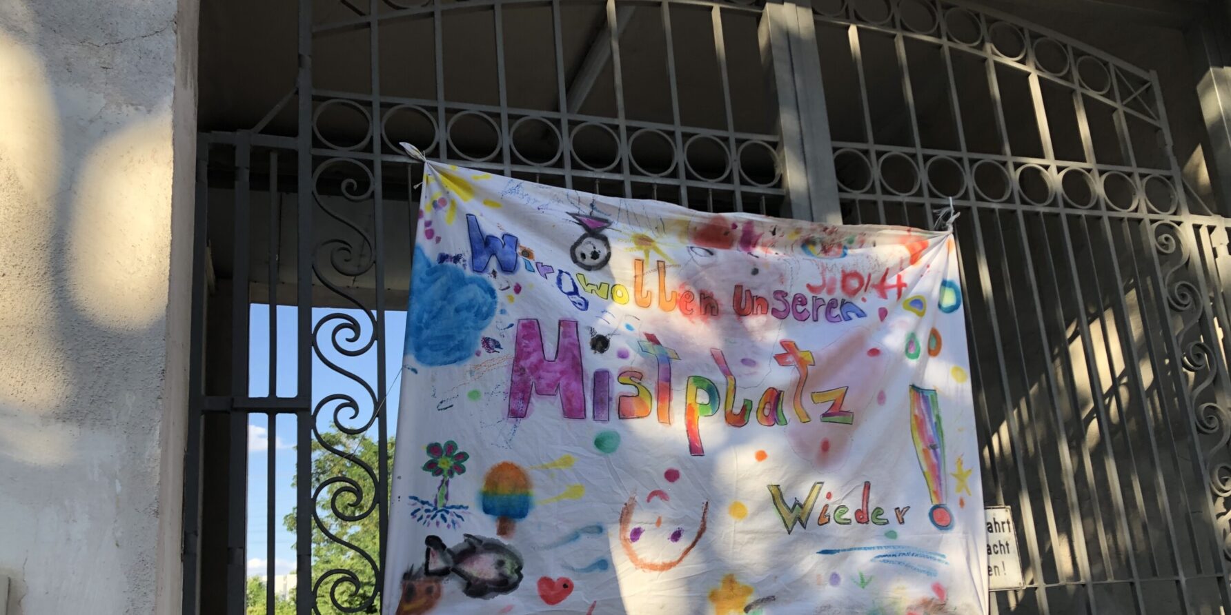Transparent am Tor des alten Mistplatzes, auf dem in bunten Farben gemalt steht: "Wir wollen unseren Mistplatz wieder"